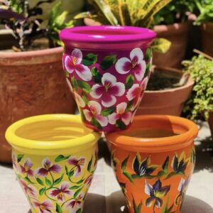Set of three hand-painted terracotta pots featuring colourful floral designs in pink, yellow, and orange.