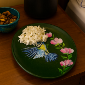 Hand-painted decorative plate featuring a bluebird in flight with pink blossoms on a deep green background featuring a blue songbird and pink blossoms on a dark green background, displayed as decorative home decor.