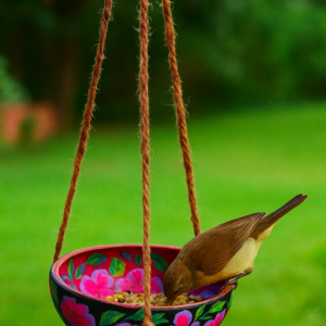 Hand-painted terracotta hanging bird feeder bowl with floral design and visiting bird in garden