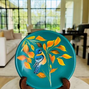 Hand-painted decorative plate featuring a blue bird among golden autumn leaves on a turquoise background